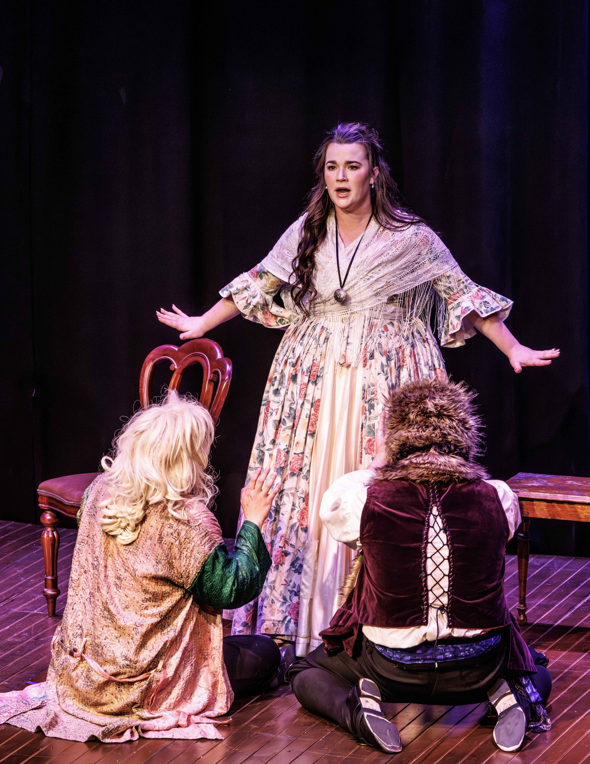 Melbourne Opera performer singing centre stage in Così fan tutte, with two other performers kneeling beside her